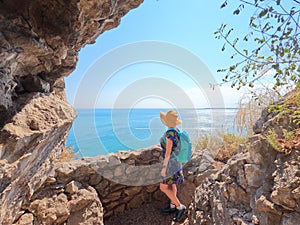 Young woman wearing a blue backpack and a hat admiring the sea view in rilkeweg, italy