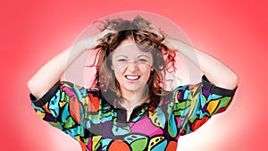 Young woman wearing bright shirt messing up her hair, big smile.