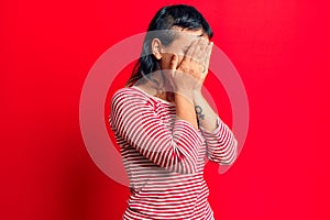 Young woman wearing casual clothes with sad expression covering face with hands while crying