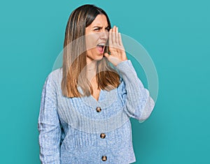 Young woman wearing casual clothes shouting and screaming loud to side with hand on mouth