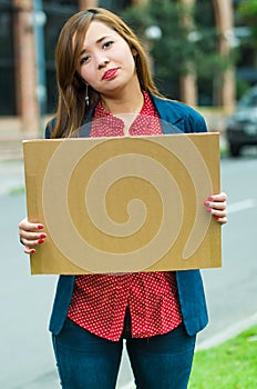 Young woman wearing casual clothes standing outdoors holding up cardboard poster, protesting concept