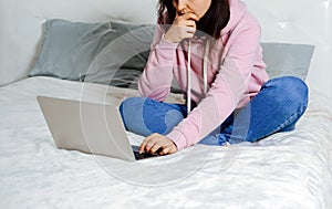 Young woman wearing casual jeans and shirt sitting on bed and using notebook. Freelance concept