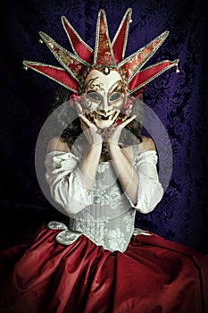 A young woman wearing a corset, a Venetian carnival mask and red skirt and sitting in an opulent, vintage setting