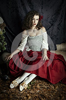 A young woman wearing a corset and red skirt and sitting in an opulent, vintage setting