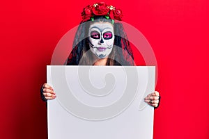 Young woman wearing day of the dead costume holding blank empty banner looking positive and happy standing and smiling with a