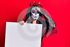 Young woman wearing day of the dead costume holding blank empty banner stressed and frustrated with hand on head, surprised and