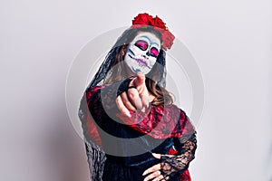 Young woman wearing day of the dead costume over white laughing at you, pointing finger to the camera with hand over body, shame