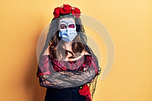 Young woman wearing day of the dead costume wearing medical mask happy face smiling with crossed arms looking at the camera
