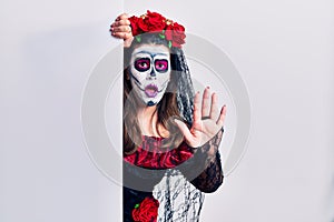Young woman wearing day of the dead custome holding blank empty banner doing stop gesture with hands palms, angry and frustration