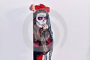 Young woman wearing day of the dead custome holding blank empty banner looking stressed and nervous with hands on mouth biting