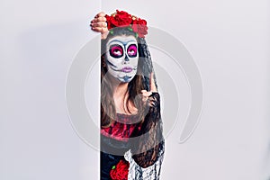 Young woman wearing day of the dead custome holding blank empty banner pointing up looking sad and upset, indicating direction