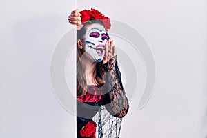 Young woman wearing day of the dead custome holding blank empty banner shouting and screaming loud to side with hand on mouth