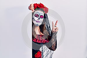 Young woman wearing day of the dead custome holding blank empty banner smiling looking to the camera showing fingers doing victory
