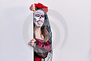 Young woman wearing day of the dead custome holding blank empty banner sticking tongue out happy with funny expression