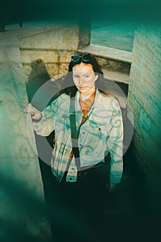 An young woman wearing a denim jacket is walking down the stairs, and the pattern from the railing casts a shadow on her face.