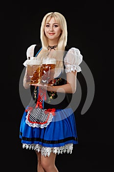 Young woman wearing a dirndl with two beer mugs on black background.