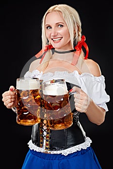 Young woman wearing a dirndl with two beer mugs on black background.