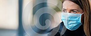 Young woman wearing disposable blue virus face mouth nose mask, closeup portrait - wide banner with space for text left side. photo