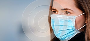 Young woman wearing disposable blue virus face mouth nose mask, closeup portrait - wide banner with space for text left side.