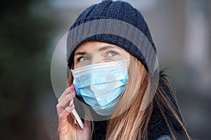 Young woman wearing disposable blue face mouth nose mask talking on mobile phone. Closeup detail, can be used during