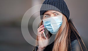 Young woman wearing disposable blue face mouth nose mask talking on mobile phone. Closeup detail, can be used during