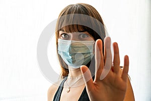 Young woman wearing disposable face mask gesturing to stop