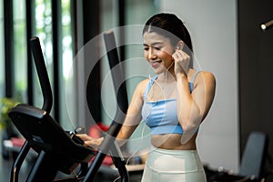 Young woman wearing earphones is choosing workout music with smart phone to listen while practicing in gym, Technology to stay fit