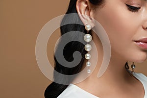 Young woman wearing elegant pearl earrings on brown background, closeup. Space for text