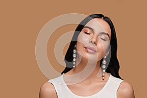 Young woman wearing elegant pearl earrings on brown background, space for text