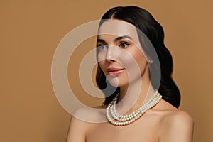 Young woman wearing elegant pearl jewelry on brown background, space for text
