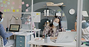 Young woman wearing face mask doing elbow bump with colleague and working with computer in office