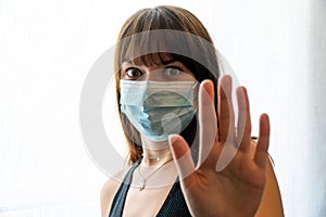 Young woman wearing face mask gesturing to stop with one hand, backing away