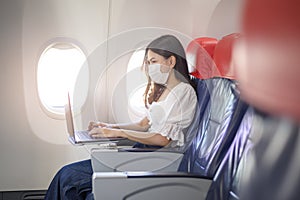 young woman wearing face mask is using laptop onboard, New normal travel after covid-19 pandemic concept