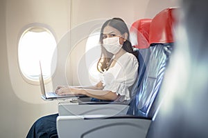 Young woman wearing face mask is using laptop onboard, New normal travel after covid-19 pandemic concept