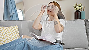 Young woman wearing glasses to read book sitting on sofa at home