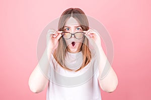 Young woman wearing glasses is very surprised looking at the camera and lowering her glasses. Surprise and shopping concept on