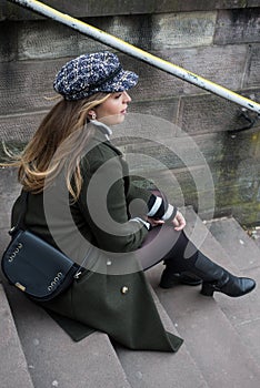 young woman wearing a greeen winter coat sitting in stairs in the street