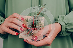 Young woman wearing green dress holding Christmas present box decorated with Christmas tree twig. Christmas holidays and New Year