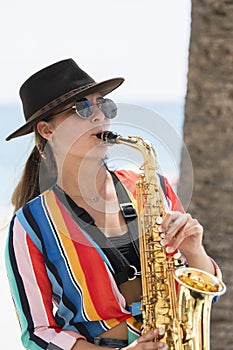Young woman wearing a hat and glasses playing a saxophone. Street performer and lifestyle concept