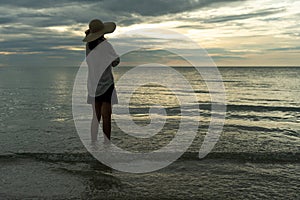 A young woman wearing a hat stands alone on an empty sandy beach by the sea. Lonely young tourists look at the horizon. The concep