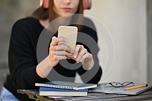 Young woman wearing headphone typing text message, chatting online on mobile phone