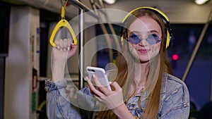 Young woman wearing headphones listening music, funny relax dancing while traveling by bus to city