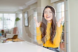 Young woman wearing headphones listening to music celebrating mad and crazy for success with arms raised and closed eyes screaming