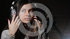 Young woman wearing headphones in recording studio near microphone