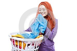 Young woman wearing hijab carrying laundry basket while smelling