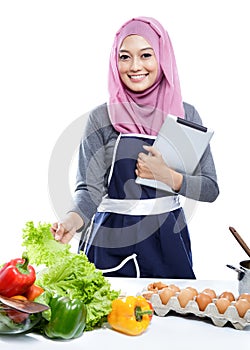 Young woman wearing hijab reading cooking recipe on tablet whil