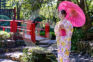 A young woman wearing a Japanese traditional kimono or yukata holding an umbrella is happy and cheerful in the park