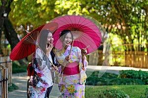 A young woman wearing a Japanese traditional kimono or yukata holding an umbrella is happy and cheerful in the park