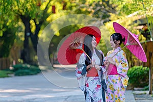 A young woman wearing a Japanese traditional kimono or yukata holding an umbrella is happy and cheerful in the park