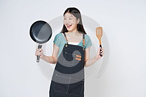 Young woman wearing kitchen apron cooking and holding pan and spatula isolated on white background